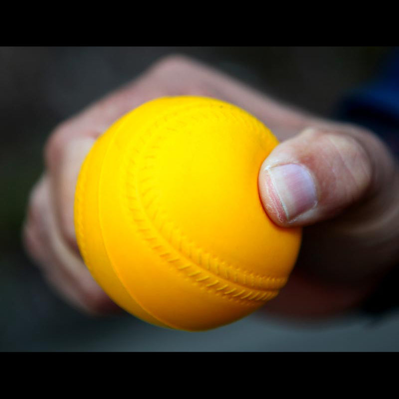 A hand holding a Bazooka yellow foam cricket machine ball.