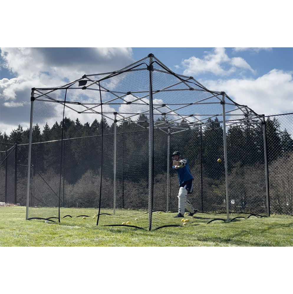 A cricketer batting inside a folding cricket net with a steel frame, set up on a grass field.