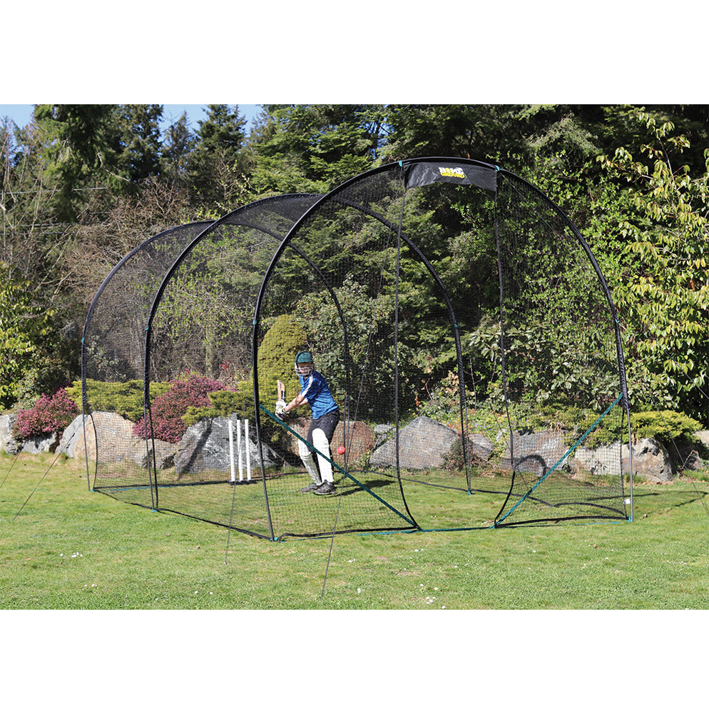 A person is practicing cricket batting inside a black colored portable cricket net set up on a grassy field.