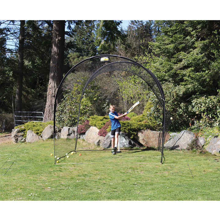 A person is practicing cricket batting against a cricket net which is set up outdoors.