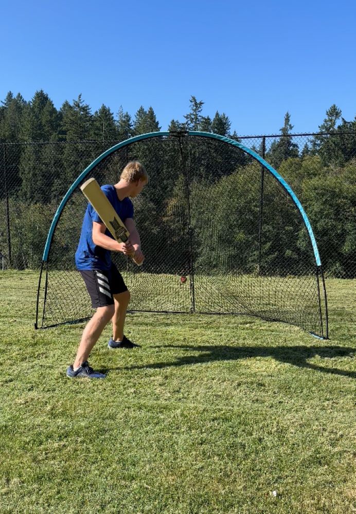 A batter playing shots against a blue and black colored dome-shaped net outdoors.