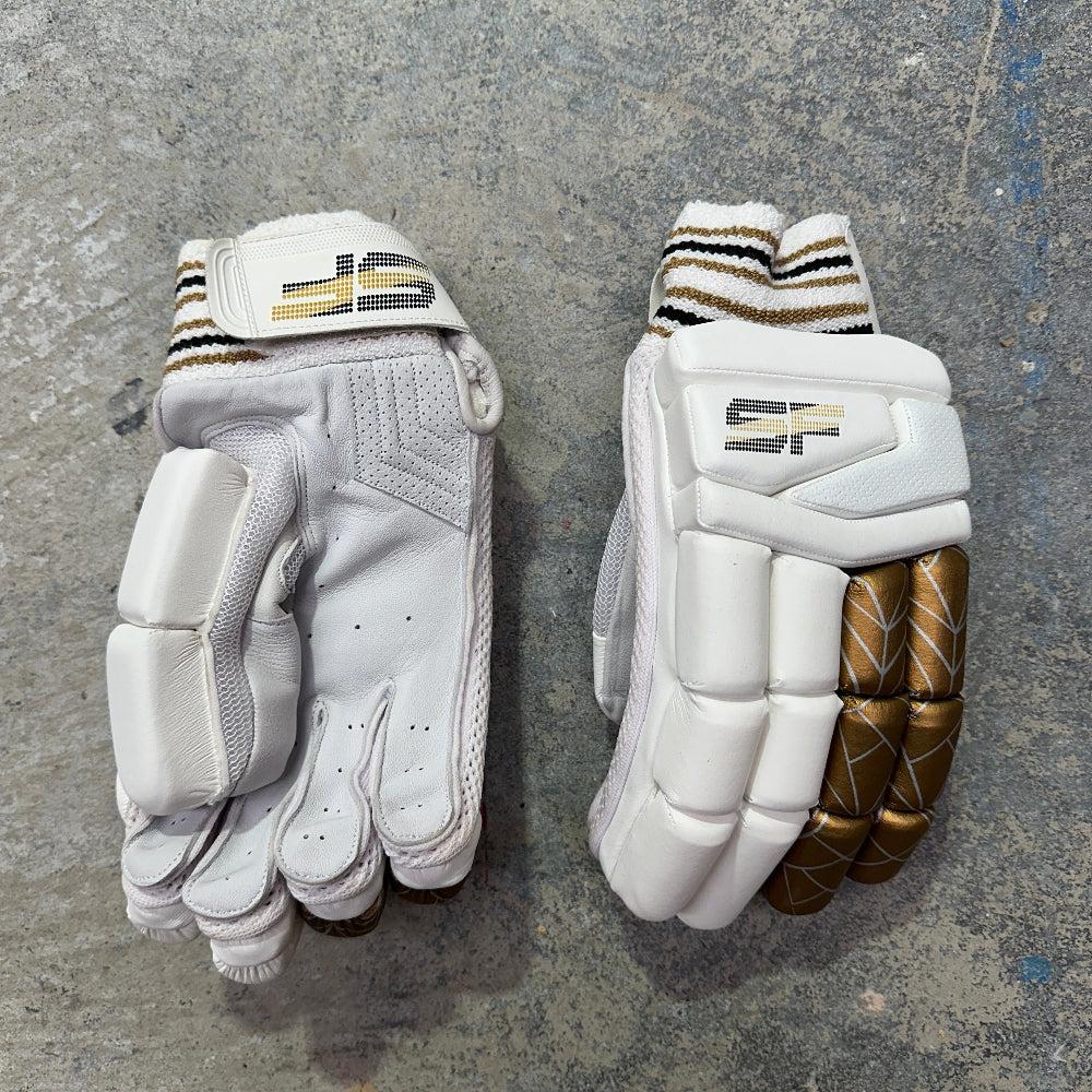 Pair of white cricket gloves with gold accents on a gray surface with SF branding