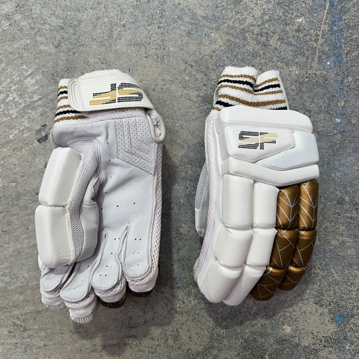Pair of white cricket gloves with gold accents on a gray surface with SF branding