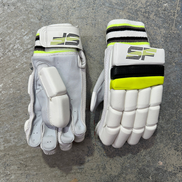 Pair of SF branded white cricket gloves with black and yellow accents on a gray surface