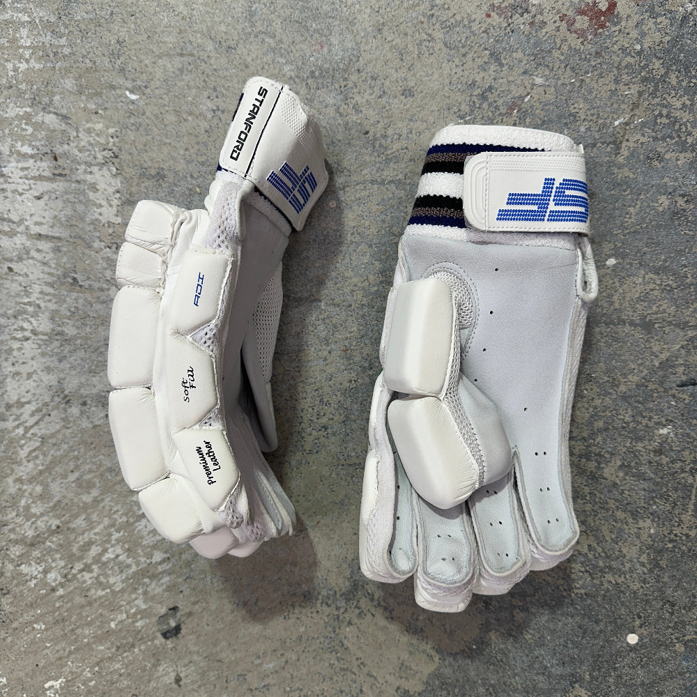 Pair of white cricket gloves with SF brand logos on a gray concrete surface
