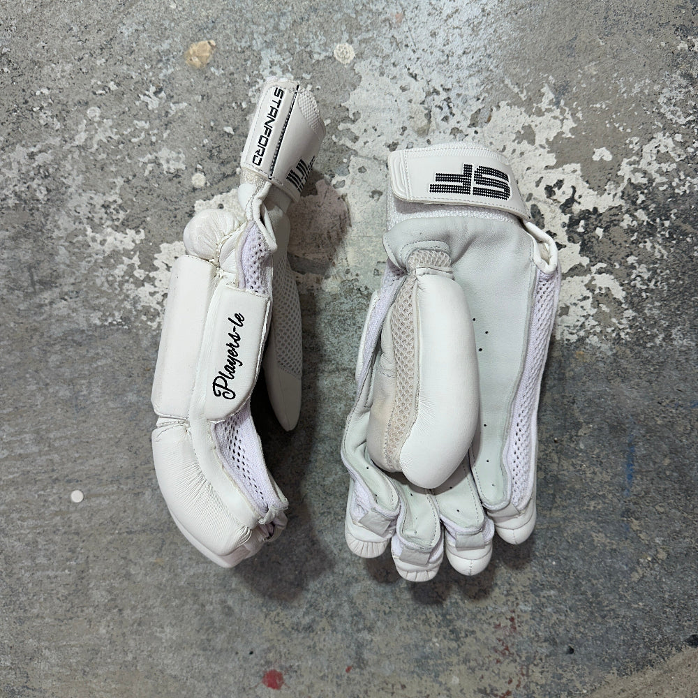 Pair of white SF cricket gloves on a textured gray surface