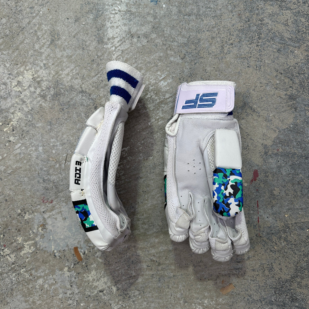 Two white SF cricket gloves with camo design on a gray surface