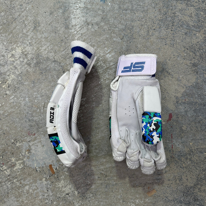Two white SF cricket gloves with camo design on a gray surface
