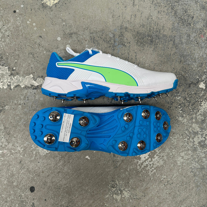 White sports shoe with blue sole and green PUMA logo on a concrete surface