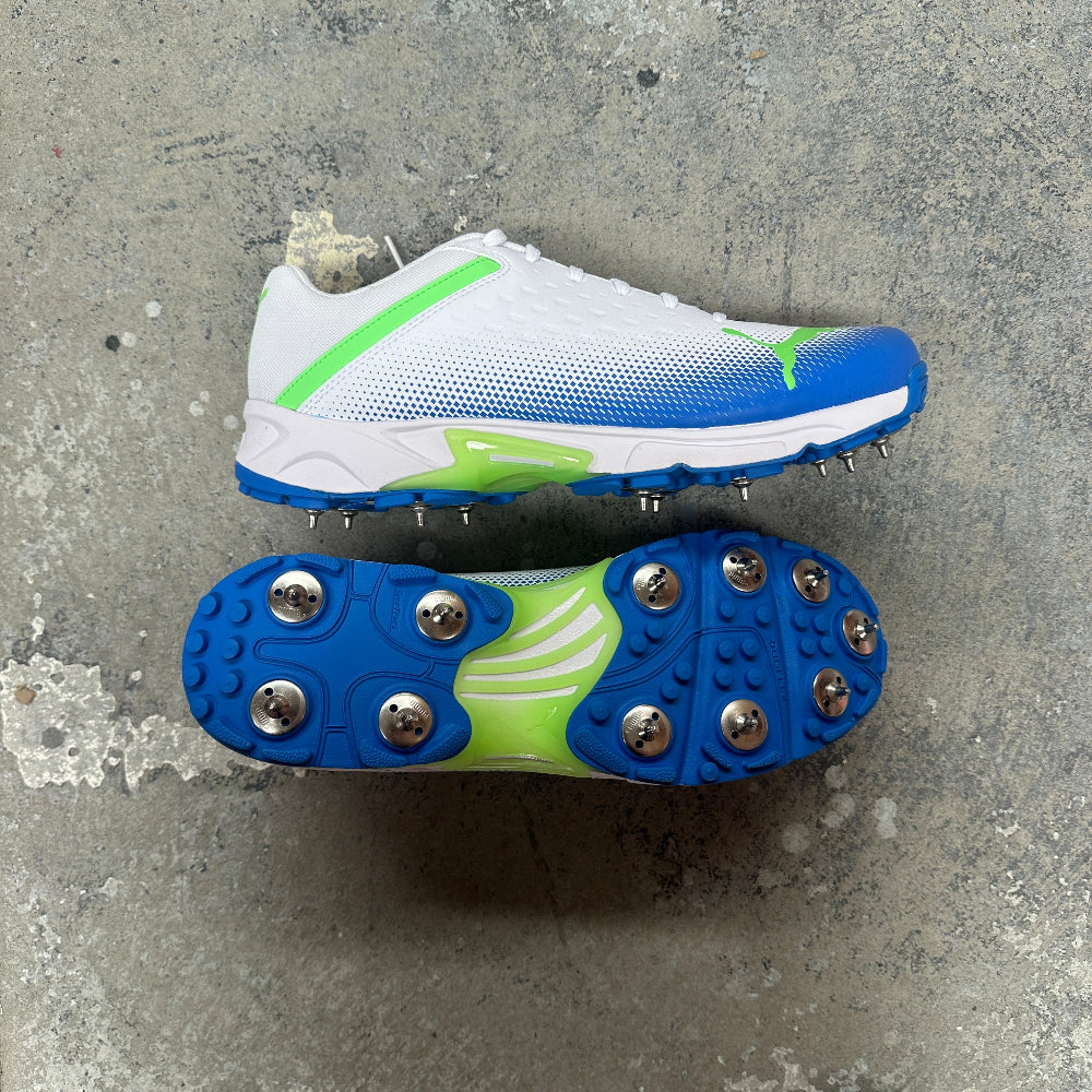 White Puma cricket spike with blue and green accents on a concrete surface