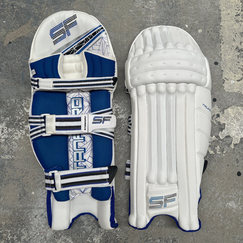 Pair of blue and white SF Triumph cricket pads on a gray surface