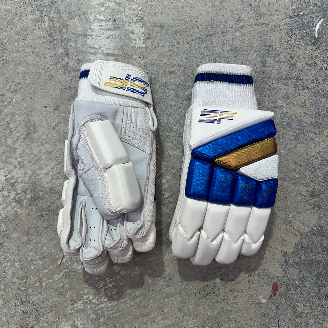 Pair of white SF cricket gloves with blue and gold accents on a gray surface