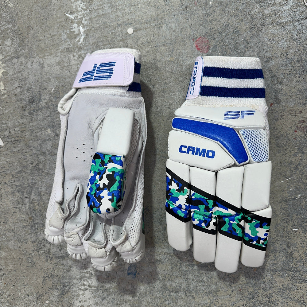Pair of white SF Camo cricket gloves with blue and green camouflage patterns on a gray surface