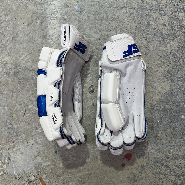 Pair of SF white and blue cricket gloves on a gray concrete surface