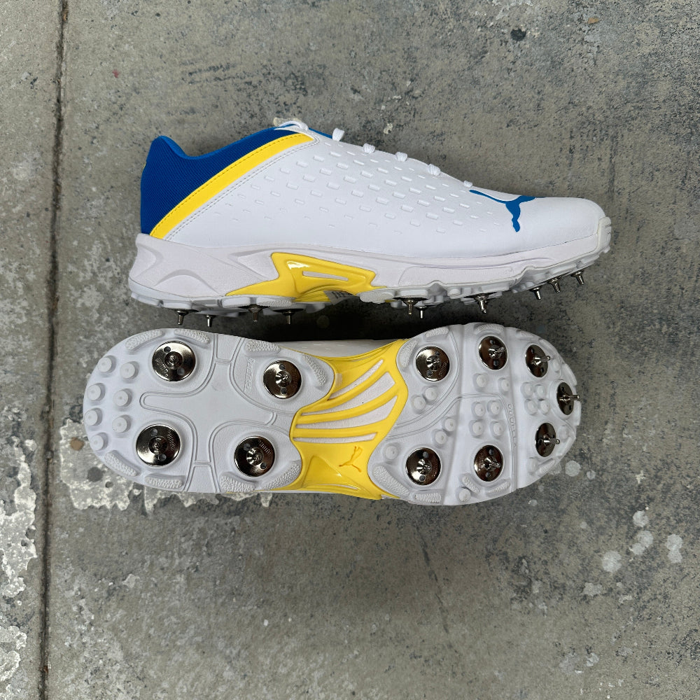 White Puma cricket spike with blue and yellow accents on a concrete surface