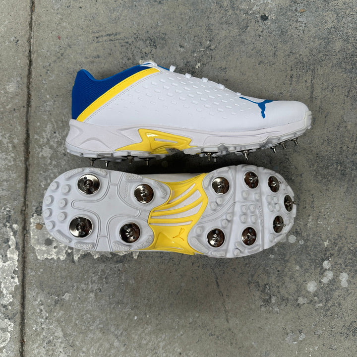 White Puma cricket spike with blue and yellow accents on a concrete surface