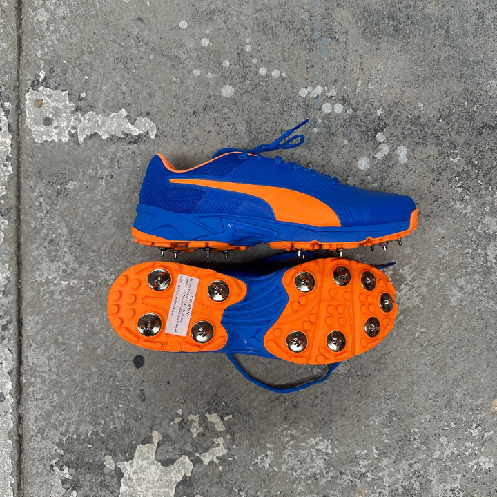 Blue and orange Puma banded cricket shoes on a concrete surface