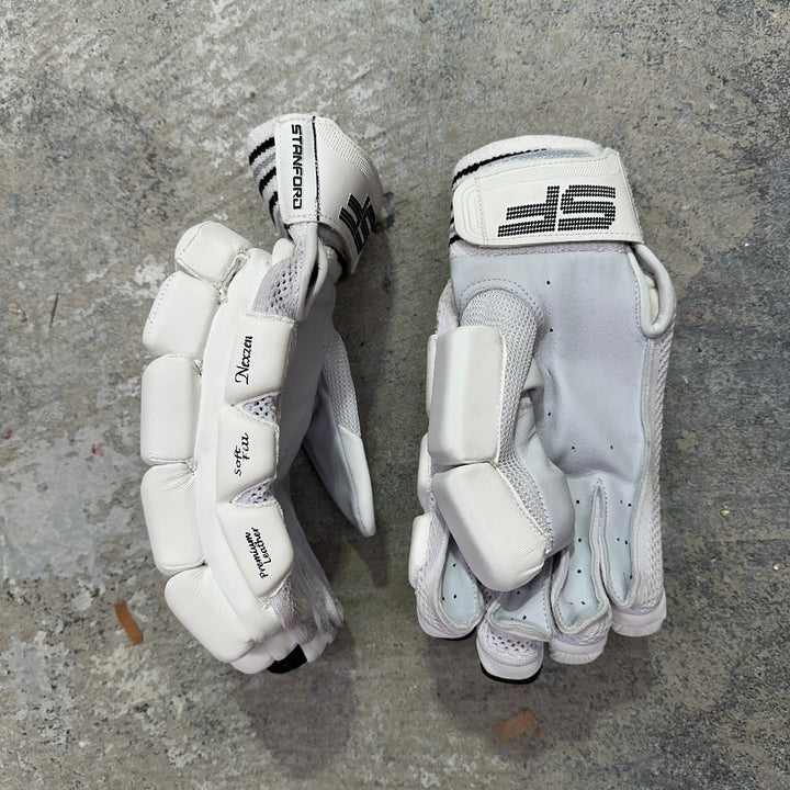Pair of white sports gloves with a black SF logo on a gray concrete surface
