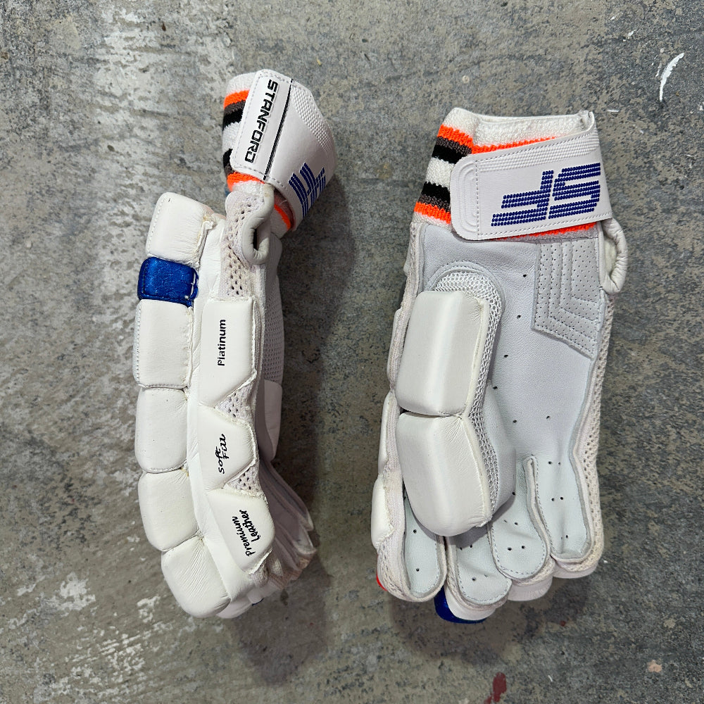 Pair of white cricket gloves with SF brand logo on a gray concrete surface