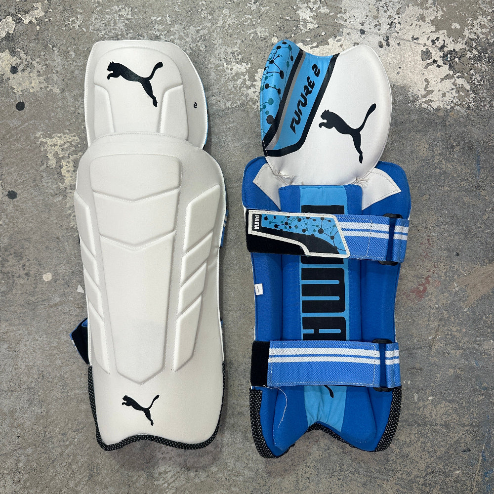Pair of white and blue shin guards with Puma logo on a textured gray background