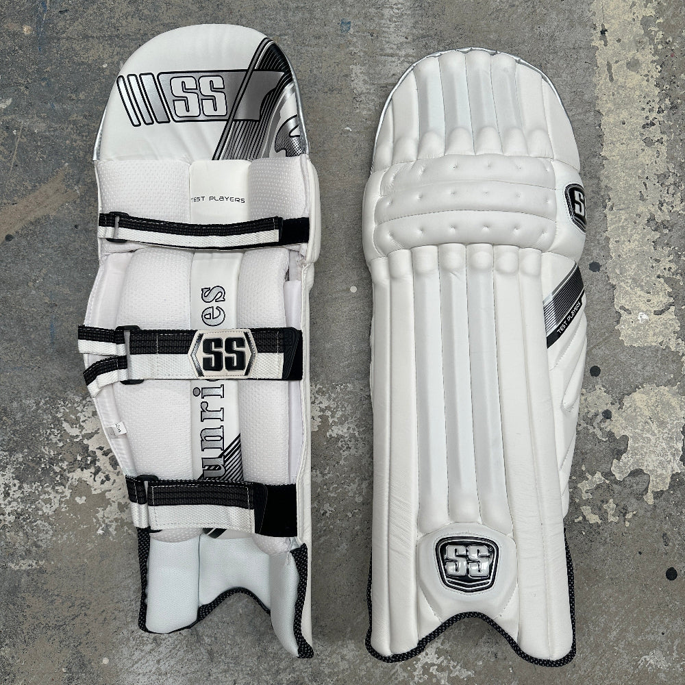 Pair of white SS cricket pads with black accents on a textured gray background
