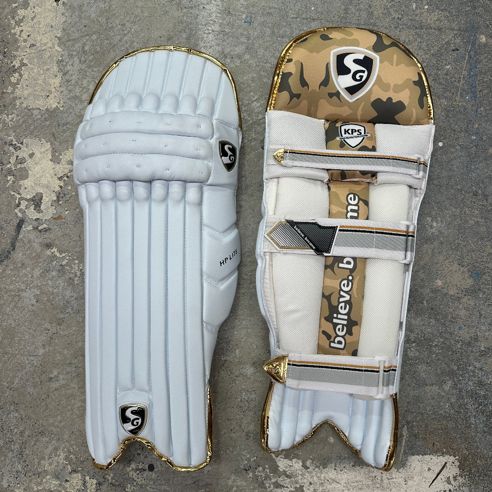 Two cricket pads, one white and one with camouflage pattern, on a textured surface with SG branding