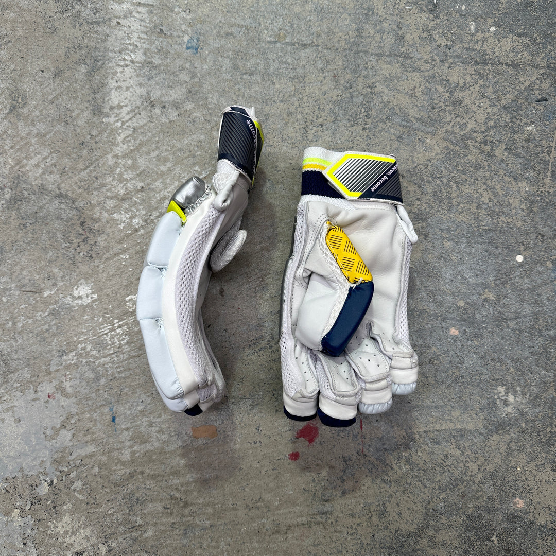 Pair of white batting gloves with black and yellow accents on a gray concrete surface