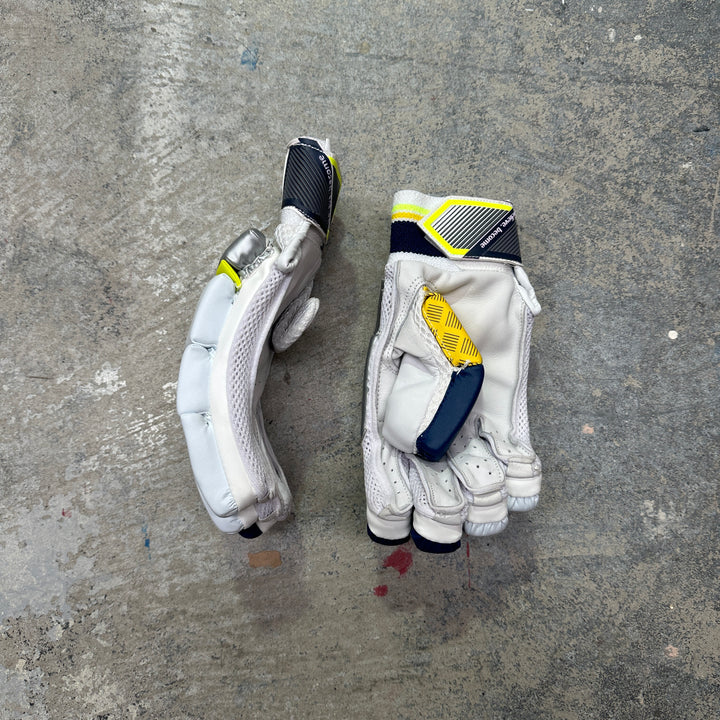 Pair of white batting gloves with black and yellow accents on a gray concrete surface