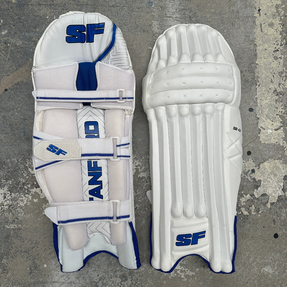 Pair of white SF cricket pads with blue accents on a gray background