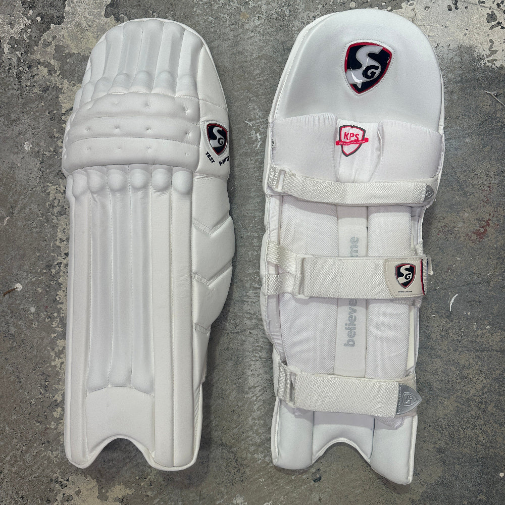 Pair of white cricket pads with visible SG branding on a gray surface