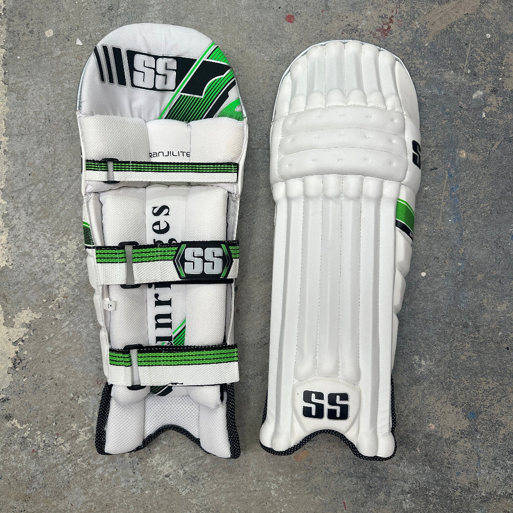 Pair of white cricket pads with green and black accents and SS branding on a gray surface