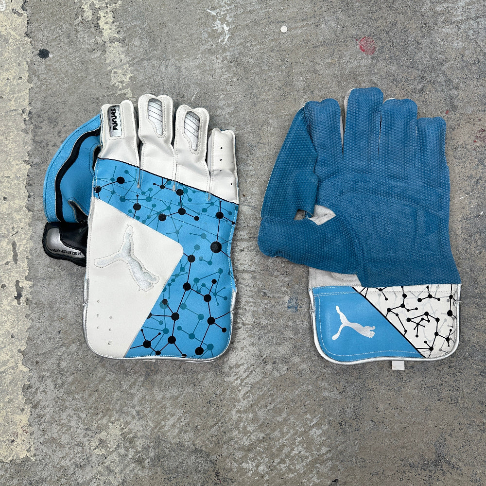 Pair of blue and white Puma wicket keeping gloves on a textured gray surface