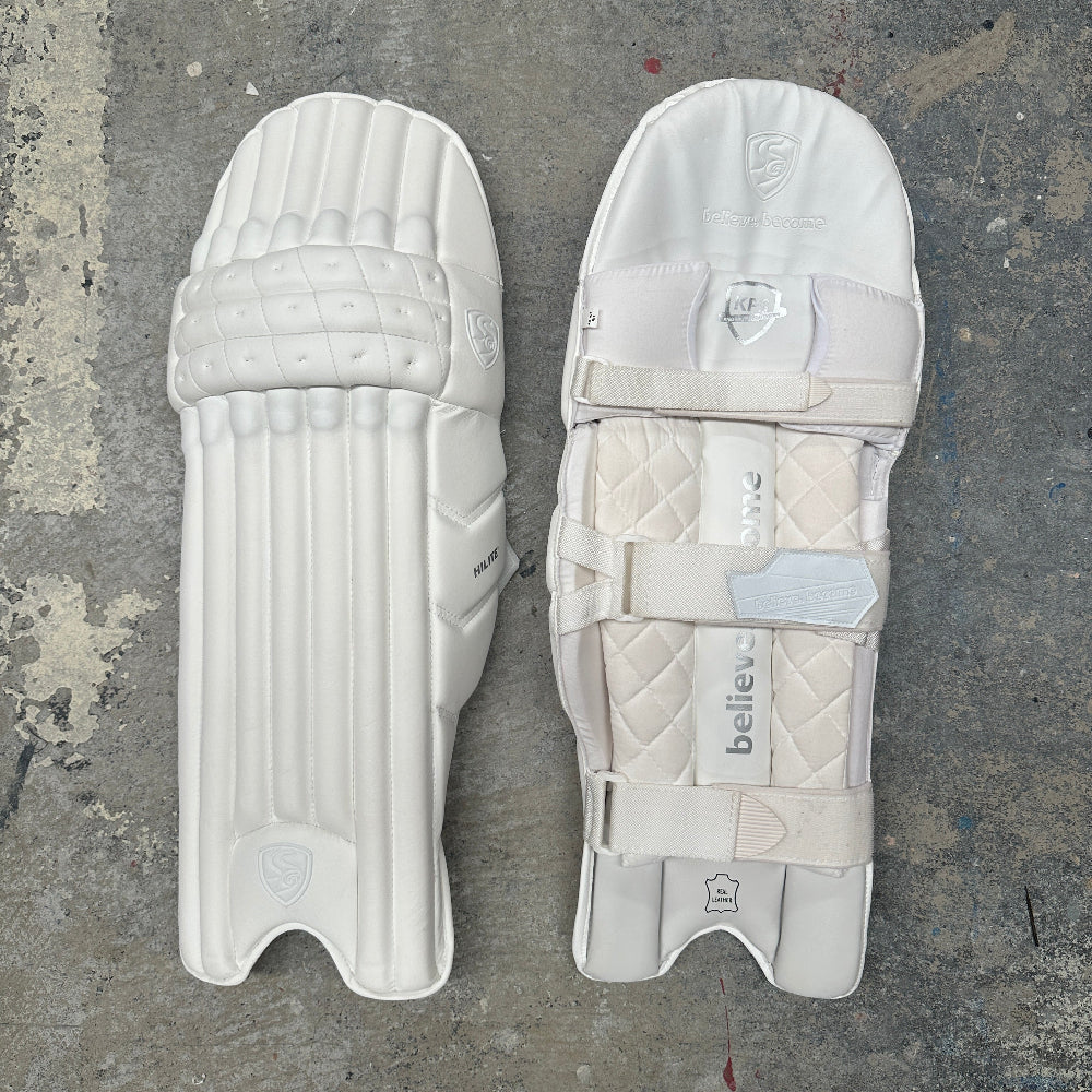 Pair of all-white SG Hilite cricket pads on a textured gray surface