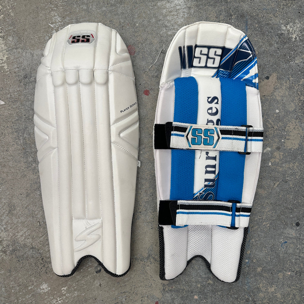 Pair of white and blue cricket pads with 'SS' branding on a gray surface