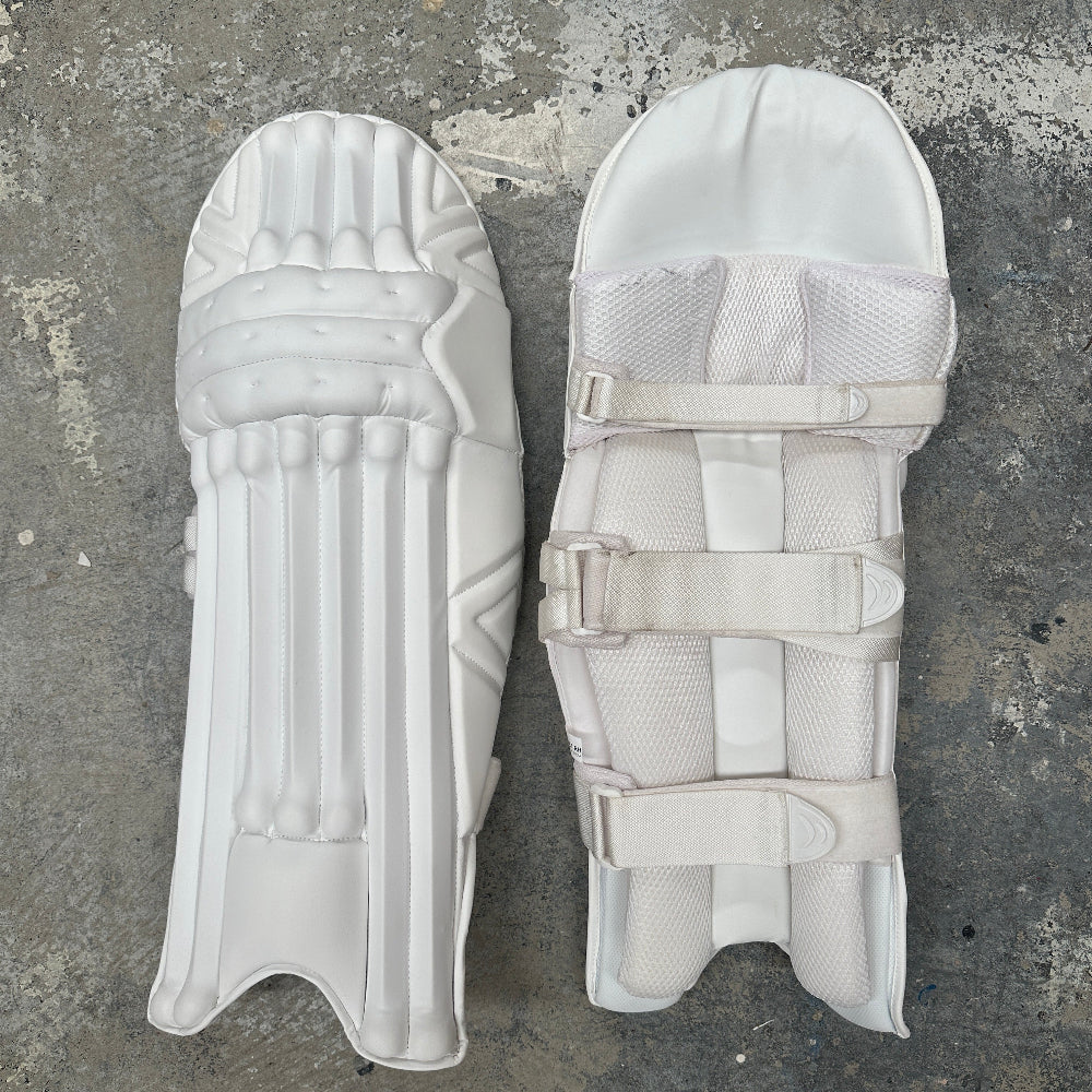 Pair of plain, all-white cricket leg guards on a gray concrete surface