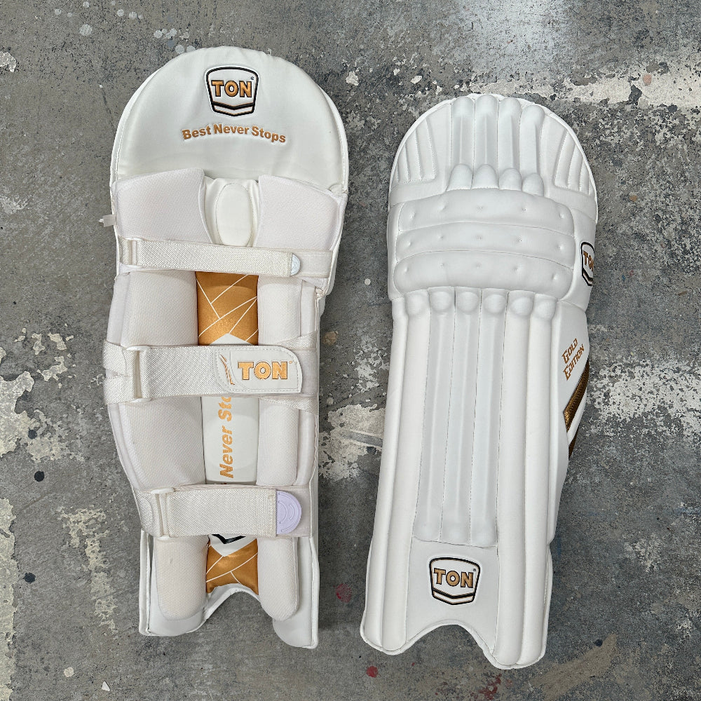 Pair of white cricket pads with 'TON' branding on a gray surface