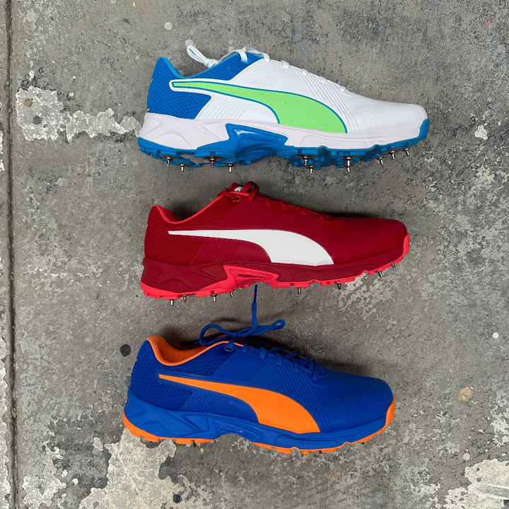 Three Puma cricket sports shoes with different color combinations on a concrete surface
